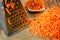 Metal grater and pile of grated carrots lie on wooden table. Coo