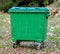 Metal green garbage can with wheels in countryside.