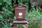 Metal mailbox with tube for newspapers mounted on fence with flowers and garden vegetation in background