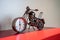 Metal motorcycle with clock on red shelf for home decoration.