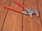 Metal plumber wrench with red handles on wooden surface