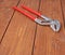 Metal plumber wrench with red handles on wooden surface