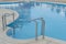 Metal pool ladder handrails of swimming pool with blue water,