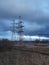 Metal pylons of a power line against a disturbing cloudy sky on the outskirts of a city. High voltage towers. Desolate