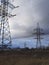 Metal pylons of a power line against a disturbing cloudy sky on the outskirts of a city. High voltage towers. Desolate