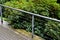 Metal railing on the edge of the park path above the slope. rope stainless steel cable railings. an evergreen rhododendron shrub g