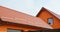 Metal roofing construction: A red metal gable roof with snow stoppers, snow guards and roof gutters of an orange painted house