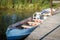 Metal row boats - one with plastic chair in it- pulled up to pier with mossy weedy pond bank behind