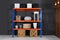 Metal shelving unit with wooden crates and different household stuff near black wall indoors