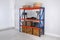 Metal shelving unit with wooden crates and household stuff near light wall indoors