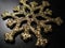 Metal snowflake with gold sequins on black background. Gold snowflake with glitter and shimmer. Christmas decorative element, toy