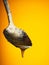 Metal spoon with natural honey on yellow background. Drop hangs from the edge of the spoon. Close-up view. Macro shots.