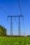 Metal supports and cables of a high-voltage transmission line over a green field in the early summer morning