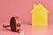 Metal tape measure funny concept. House renovation. Home repair and redecorated concept. Yellow house shaped figure on pink