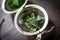 Metal tea infuser with dried leaves of green tea and fresh mint on a dark brown wooden background