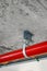 Metal tube pole or pipe clamp hanging on concrete ceiling holding red metal pipe