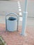 Metal urn near the road. A metal trash can is standing near a pillar on the sidewalk. Forging of garbage cans stands near a bench
