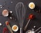 Metal whisk, spoon with red pepper knife and halved boiled eggs on a black concrete background. Cooking Concept. Flat