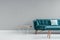 Metal and wood end table with book standing next to turquoise sofa with pillow in real photo of grey living room interior with pla