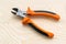 Metall wire cutters with orange black rubber handles on a rough wooden background. Electrician tool for repair and construction