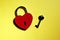 Metallic red heart shaped lock and key on yellow background