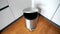 Metallic trash can on the parquet floor in a kitchen near of kitchen furniture