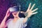 Metaverse. Blurry portrait of young happy woman in VR glasses with reaches hand. Dark neon mesh background. The concept