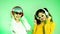 Metaverse music world concept, two young asian woman wearing headphone listen to music and dancing on the green background