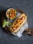 Mexican street style hot dog with corn salsa on a wooden cutting board on dark background