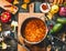 Mexican vegetarian bean soup in cooking pot with ladle on rustic kitchen table ingredients and cutting board, top view.