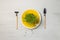 Micro-greenery in a pot on a bright yellow plate and miniature gardening tools. Top view on a gray wooden background