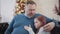 Mid-adult father and little daughter sitting on couch with Christmas tree at the background and talking. Portrait of