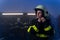 Mid adult female firefighter putting on helmet indoors in fire station at night.