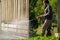 Mid adult man cleaning a wooden gate with a power washer. High water pressure cleaner used to DIY repair garden gate.