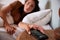 Mid adult woman waking up in bed, reaching out to smartphone on the bedside table in the foreground