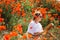 Mid-aged woman reading a book in a field of red poppies in spring flowers mood.