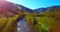 Mid air flight over fresh mountain river and meadow at sunny summer morning. Rural dirt road below.