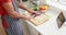 Mid section of biracial man in apron chopping vegetables and using tablet in kitchen, slow motion