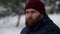Mid shot serious and bearded man with blurred snow city streets. Slo mo male serious scandinavian citizen wearing hat