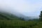 Mid summer. Morning foggy in the foothills. Beautiful summer rural landscape, lush green grass and trees