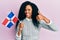 Middle age african american woman holding dominican republic flag smiling happy and positive, thumb up doing excellent and