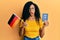 Middle age african american woman holding germany flag and passport afraid and shocked with surprise and amazed expression, fear