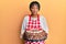 Middle age african american woman wearing baker apron holding homemade cake relaxed with serious expression on face