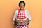 Middle age african american woman wearing baker apron holding homemade cake smiling with a happy and cool smile on face