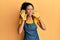 Middle age african american woman wearing professional apron trying to hear both hands on ear gesture, curious for gossip