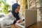 Middle age Asian Indonesian Muslim woman in traditional hijab head scarf working relaxed at home garden running online business