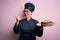 Middle age baker woman wearing cooker uniform and hat holding tray with delicious cake pointing and showing with thumb up to the