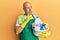 Middle age bald man wearing cleaner apron holding cleaning products serious face thinking about question with hand on chin,