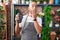 Middle age bald man working at florist shop holding dataphone covering mouth with hand, shocked and afraid for mistake