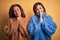Middle age beautiful couple of sisters wearing casual sweater over isolated yellow background praying with hands together asking